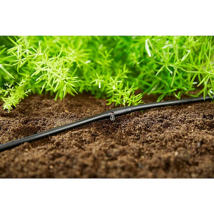 Gardena Micro-Drip Tropfrohr - Geeignet für: Randbewässerung, Anwendungsbereich: Außen, Länge: 15 m - Nahaufnahme einer Tropfbewässerungsleitung mit einem Wassertropfen, eingebettet in Erde, mit grünen Pflanzen im Hintergrund.