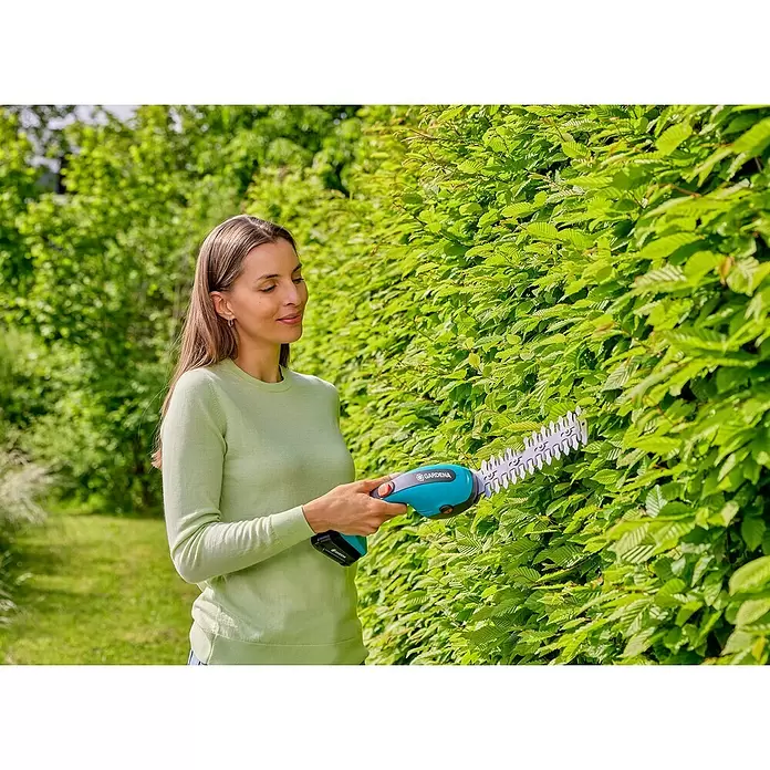 Gardena Power for All 18V Akku-Gras- & Strauchschere 20/18V P4A - 18 V, Li-Ionen, 1 Akku - Frau trimmt mit einer blau-grauen GARDENA Heckenschere eine grüne Hecke.