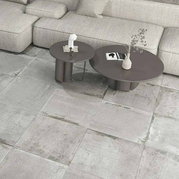 Feinsteinzeugfliese Bond Ash - 60 x 60 cm, Grau, Matt - Ein modernes Wohnzimmer mit grauen Bodenfliesen, einem Sofa und zwei Couchtischen, die eine stilvolle Atmosphäre schaffen.