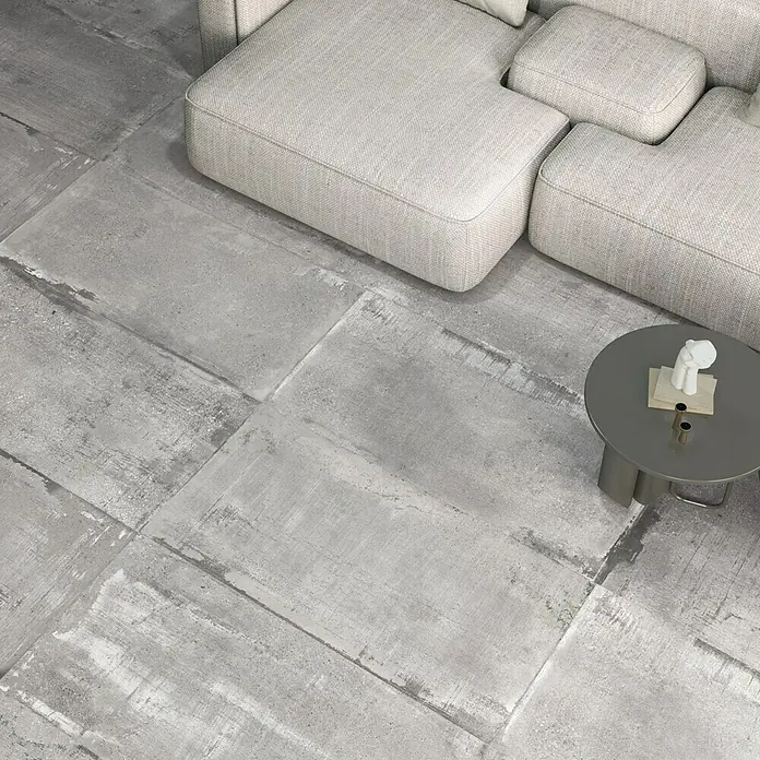 Feinsteinzeugfliese Bond Ash - 60 x 120 cm, Grau, Matt - Ein elegantes Wohnzimmer mit Betonfliesen und einer grauen Couch, die das moderne Ambiente des Raumes hervorheben. Ein stilvoller Couchtisch ergänzt das Design.
