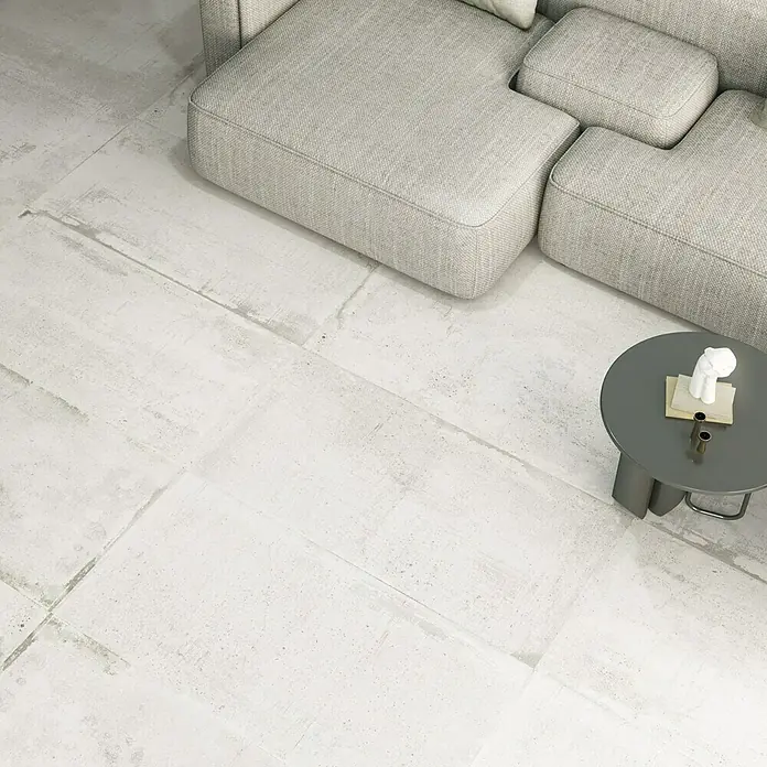 Feinsteinzeugfliese Bond - 60 x 120 cm, Weiß, Matt - Detailaufnahme eines Wohnzimmers mit hellem Sofa, Tisch und Bodenfliesen in Betonoptik.