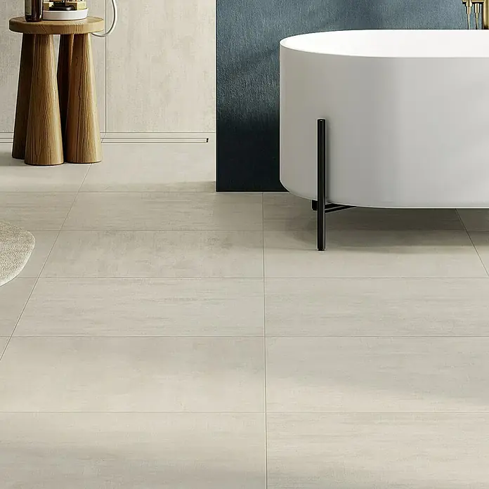 Atlas Concorde Solution Yorkshire Feinsteinzeugfliese Almond - 60 x 60 cm, Beige, Matt - Nahaufnahme eines Badezimmers mit hellen Fliesen, einem Holzhocker und einer weißen Badewanne.