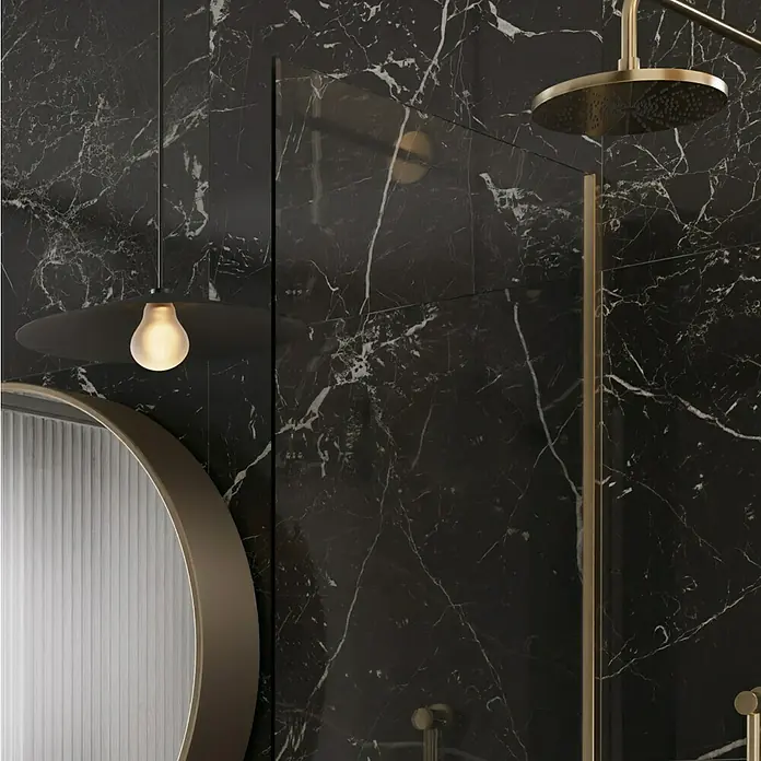 Feinsteinzeugfliese Sombra - 59,7 x 59,7 cm, Schwarz, Glänzend - Nahaufnahme einer luxuriösen Badezimmerausstattung mit einer Regendusche, einer Pendelleuchte und einem runden Spiegel vor einer Marmorwand.