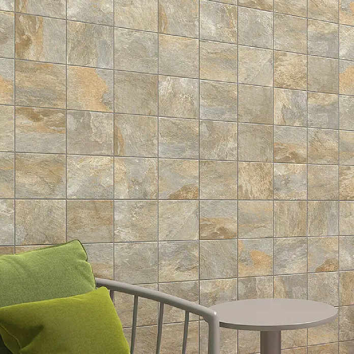 Decocer by Cinca Feinsteinzeugfliese Splash Grege - 15 x 15 cm, Braun, Matt - Nahaufnahme einer Wand, die mit quadratischen Natursteinfliesen in Beige- und Brauntönen verkleidet ist und eine rustikale Optik erzeugt.