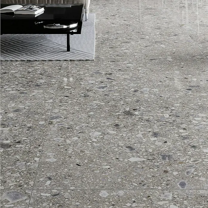 Feinsteinzeugfliese Terrazzo Ceppo - 59,7 x 119,7 cm, Graphit, Glänzend - Nahaufnahme eines grauen Terrazzobodens mit einem Couchtisch und Büchern darauf, der einen modernen Stil zeigt.