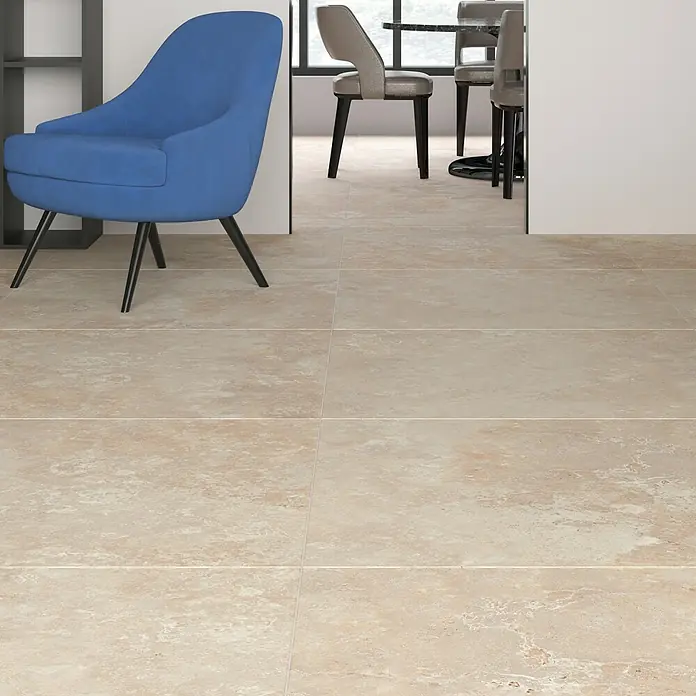 Feinsteinzeugfliese Camarque - 100 x 100 cm, Creme, Matt - Ein hellbeiger Fliesenboden erstreckt sich unter einem blauen Sessel und grauen Stühlen, der die Eleganz und Wärme der Fliesen betont.