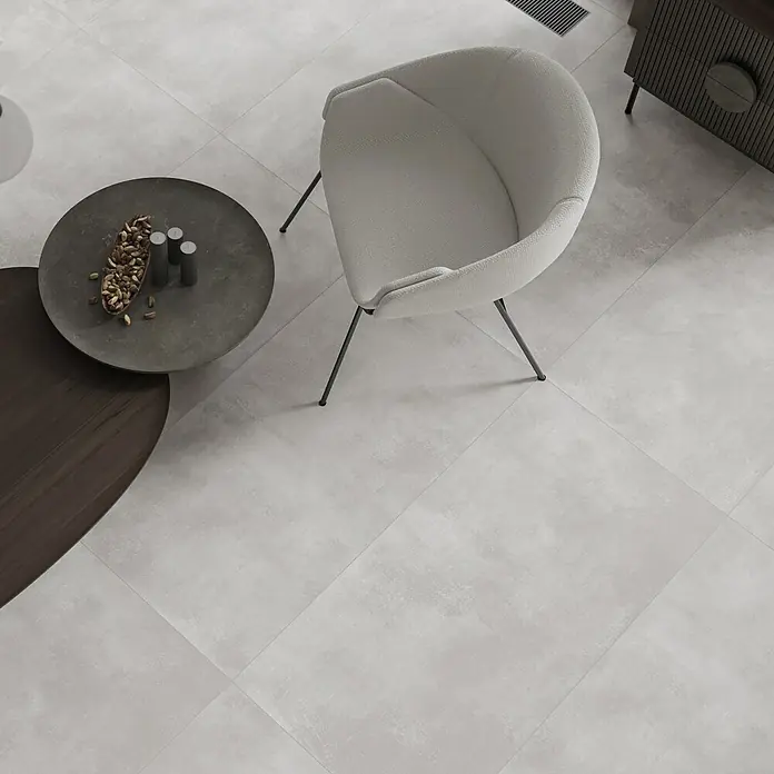 Feinsteinzeugfliese Big Show XXL - 59,8 x 119,8 cm, Grau, Matt - Elegantes Interieur mit hellgrauem Sessel, runden Tischen und Fliesenboden, das moderne Design und Komfort vereint.