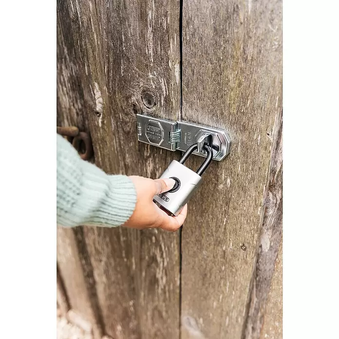 Abus Vorhängeschloss EVEROX 61/50 - Silber, 23 x 50 x 95 mm - Silbernes smartes Vorhängeschloss mit schwarzem Bügel und Fingersensor, von einer Hand gehalten, das eine silberne Überfalle an einer Holztür sichert.