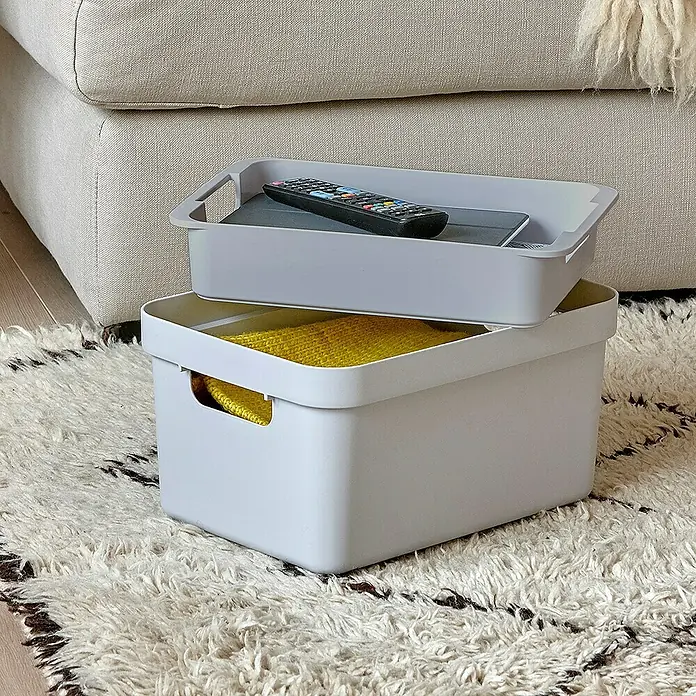 Sunware Einsatz Sigma Home M - Passend für: Sigma Home Aufbewahrungsbox 9 l/ 13 l/ 18l/ 24 l/ 25 l/ 32 l, Kunststoff - Zwei graue Aufbewahrungsboxen, die übereinander auf einem gemusterten Teppich stehen, enthalten eine Fernbedienung und eine gelbe Strickware.