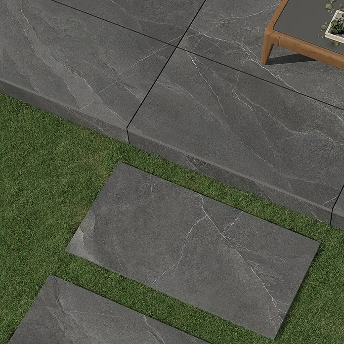 Terrassenfliese Monte 2.0 - 39,7 x 79,7 x 2 cm, Anthrazit, Matt - Graue Fliesen mit Marmorierung auf Rasen verlegt. Eine stilvolle und moderne Gartengestaltung mit robusten Bodenfliesen für den Außenbereich.