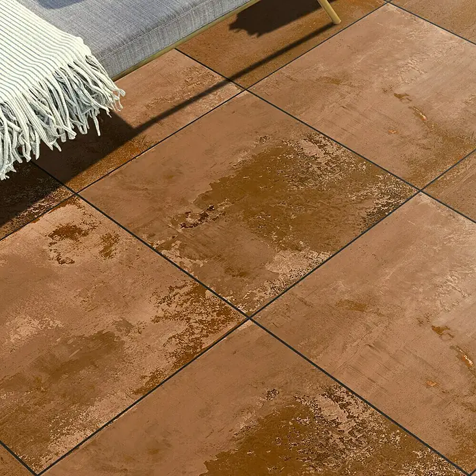 Terrassenfliese Metallic 2.0 - 60 x 120 x 2 cm, Kupfer, Matt - Nahaufnahme von quadratischen, rostfarbenen Bodenfliesen mit dunklen Fugenlinien, die eine rustikale und warme Atmosphäre schaffen.