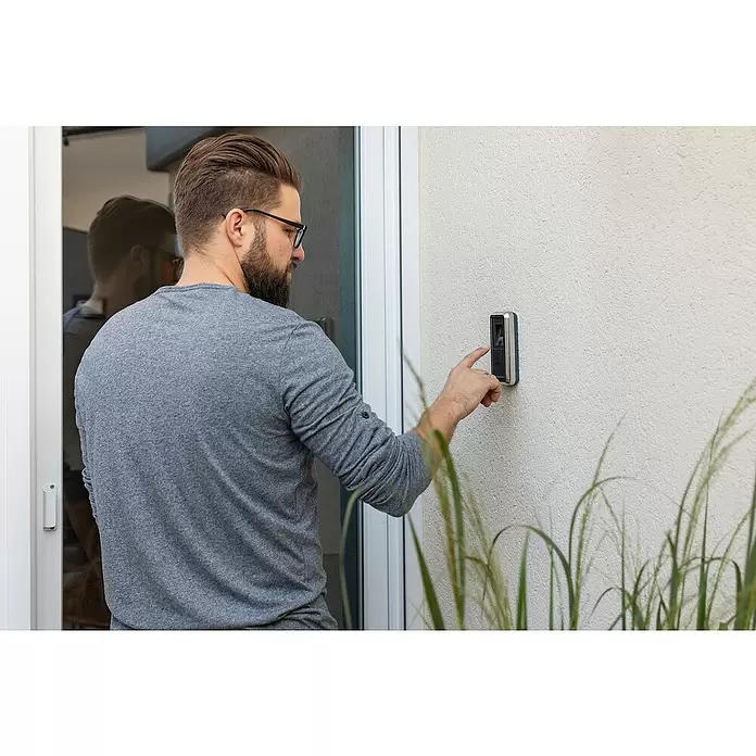 Abus HomeTec Pro Fingerabdruck Lesegerät CFS3100S - L x B x H: 29 x 67 x 143 mm, Schwarz / Silber - Ein Mann scannt seinen Finger an einem metallisch-schwarzen Smart-Zutrittskontrollgerät mit Fingerabdruckscanner neben einer Tür.