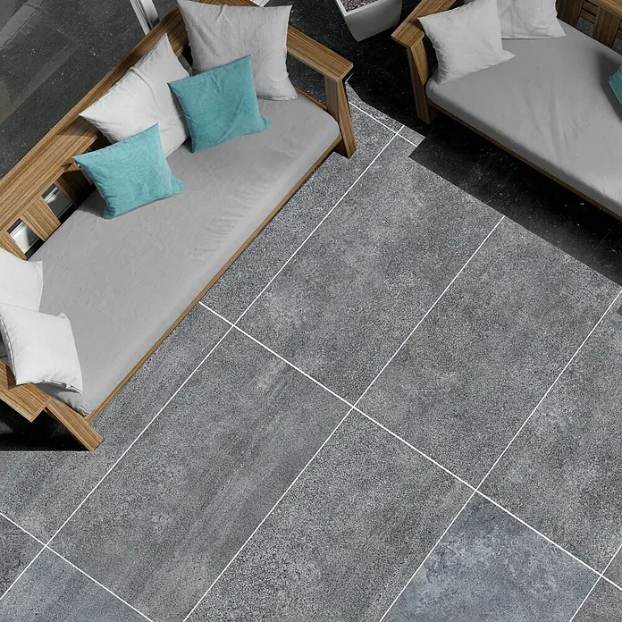 RAK Ceramics Terrassenfliese Opificio 2.0 - 60 x 120 x 2 cm, Grau, Matt - Blick von oben auf zwei graue Sofas mit hellblauen und weißen Kissen auf einem stilvollen, gefliesten Boden. Entspannung im Freien.