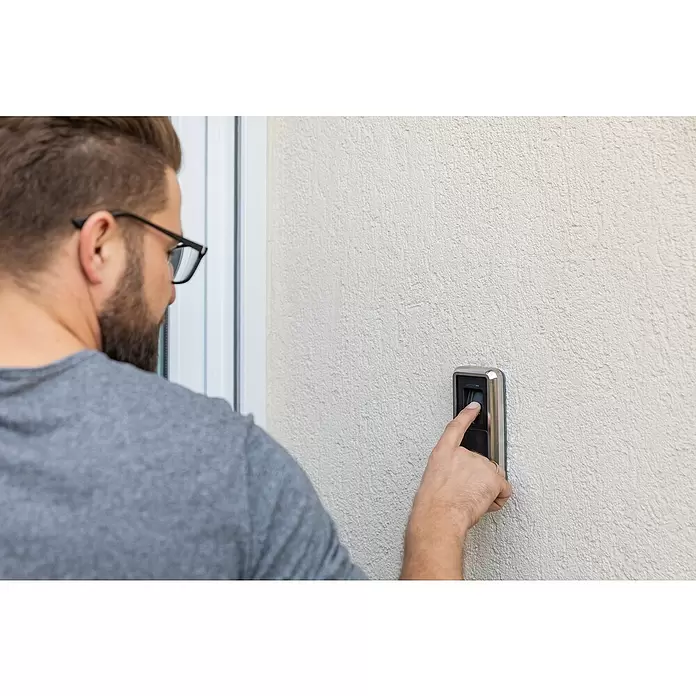 Abus HomeTec Pro Fingerabdruck Lesegerät CFS3100S - L x B x H: 29 x 67 x 143 mm, Schwarz / Silber - Ein Mann nutzt einen silber-schwarzen Fingerabdruckscanner an einer Wand zur Zutrittskontrolle.