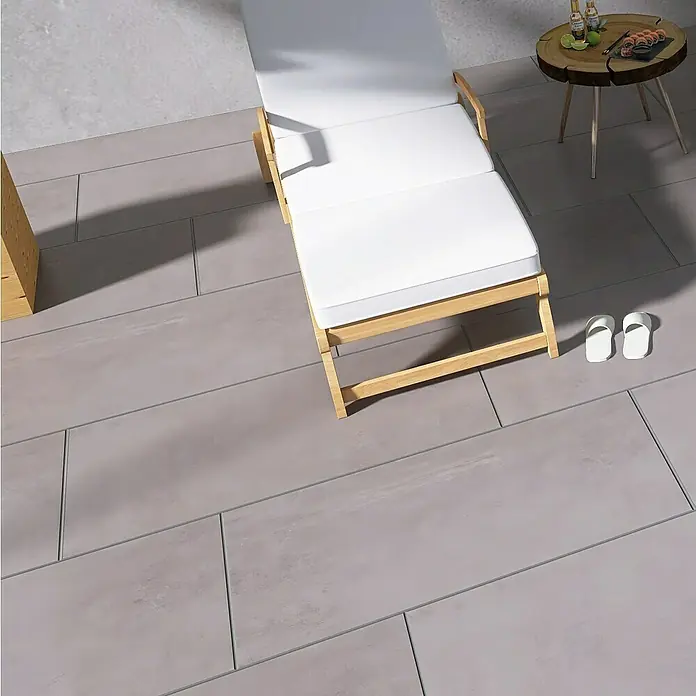 Terrassenfliese Modena - 60 x 120 x 2 cm, Ash/Graubraun, Matt - Einladende Szene mit einer stilvollen Sonnenliege aus Holz, ideal zum Entspannen im Freien, ergänzt durch einen kleinen Beistelltisch und lässige Flip-Flops.