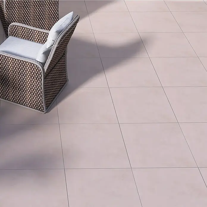 Terrassenfliese Modena - 60 x 60 x 2 cm, Mud/Beigegrau, Matt - Nahaufnahme eines gewebten Sessels mit Kissen auf einem gefliesten Boden, der die Textur und das Design des Sessels hervorhebt.