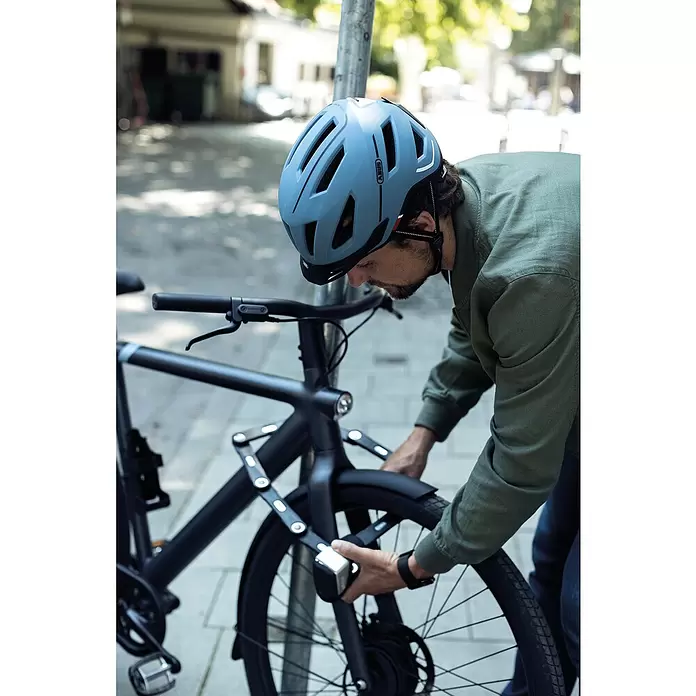 Abus Faltschloss BORDO™ One 6500A/110 - Länge: 110 cm - Person trägt einen blauen Fahrradhelm und sichert ein schwarzes Fahrrad mit einem schwarzen Faltschloss.
