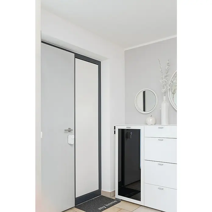 Abus Elektronisches Türschloss LOXERIS CFA4100 W - Bedienung: Über App, Geeignet für: Türen, Weiß - Helle Inneneinrichtung mit einer modernen Tür und einem weißen Schuhschrank, der mit dekorativen Spiegeln und einer Vase geschmückt ist.