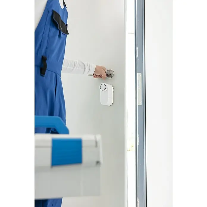 Abus Elektronisches Türschloss LOXERIS CFA4100 W - Bedienung: Über App, Geeignet für: Türen, Weiß - Ein Handwerker mit einem blauen Overall öffnet eine Tür mit einem intelligenten Türschloss, das an der Tür angebracht ist.