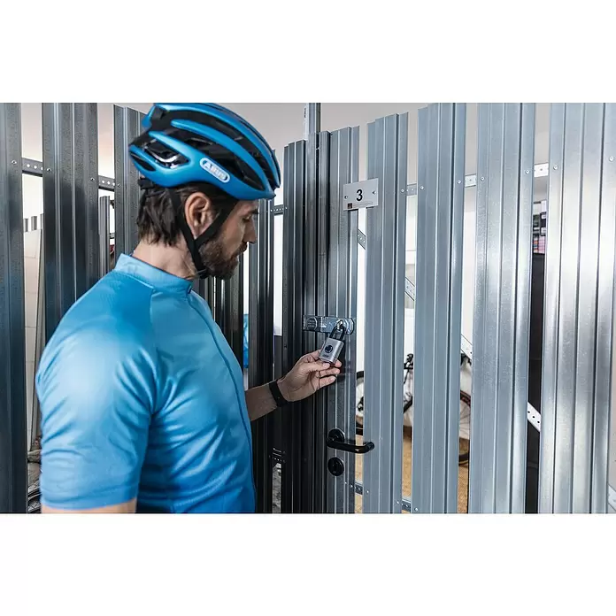 Abus Vorhängeschloss EVEROX 61/45 - SIlber, 23 x 45 x 95 mm - Mann sichert eine metallene Fahrradbox mit einem intelligenten Vorhängeschloss.