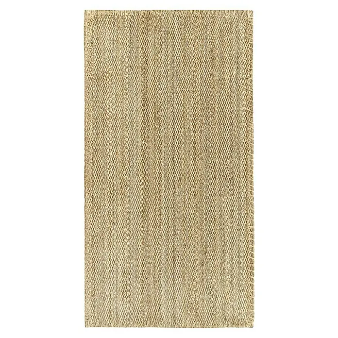 Alfombra de yute Córdoba - Natural, 150 x 80 cm, 100% yute - Primer plano de una alfombra rectangular de color marrón claro que muestra una textura tejida sobre un fondo oscuro.