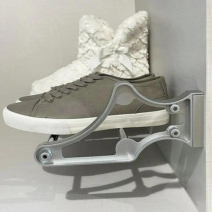 Emuca Schuhregal - Breitenverstellung: 560 mm - 1.000 mm, Silber - Diese Aufnahme zeigt einen grauen Sneaker, der auf einer modernen Schuhhalterung aus Metall platziert ist. Im Hintergrund ist ein flauschiger, weißer Stiefel zu sehen.