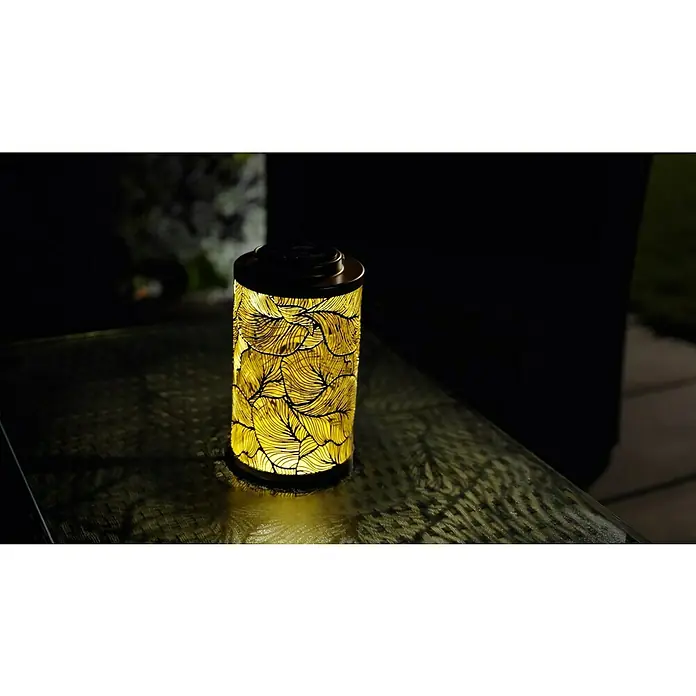 BAUHAUS Solar-Tischleuchte Dekolaterne - Gold - Dekorative Solarleuchte mit filigranem Blättermuster, die warmes Licht auf einer gemusterten Oberfläche verbreitet und eine stimmungsvolle Atmosphäre schafft.