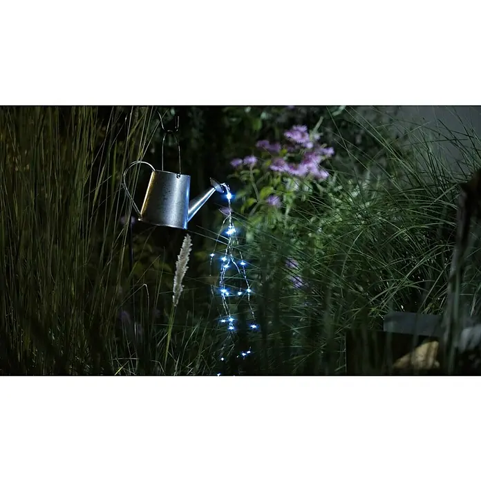 BAUHAUS Solar-Dekoleuchte Gießkanne auf Erdspitz - 0,06 W, L x B x H: 30 x 17 x 112 cm, Schwarz/Silbergrau, IP44 - Eine dekorative, silberfarbene Gießkanne mit Lichterketten, die wie Wasser aus dem Ausguss fließen, hängt im Garten.