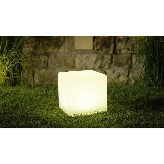 LED-Solar-Würfelleuchte - 30 x 30 x 30 cm - Quadratische LED-Leuchte strahlt warmes Licht auf einer Rasenfläche vor einer Steinmauer aus und sorgt für stimmungsvolle Beleuchtung.