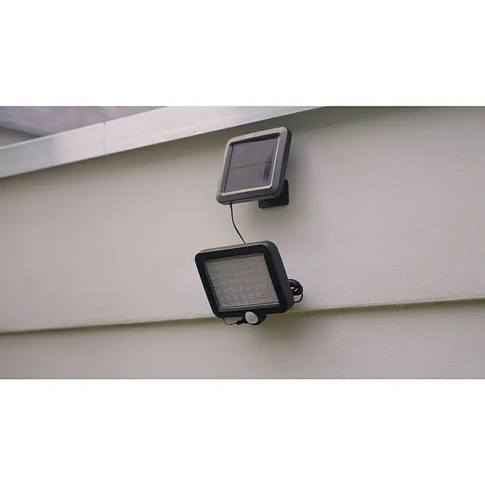 BAUHAUS Solar-Außenwandleuchte - 3 W, Schwarz, IP44, 300 lm - Bild einer Solar-Sicherheitsleuchte, die an einer Wand montiert ist und über ein Solarpanel und einen Bewegungssensor verfügt.