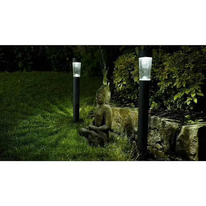 BAUHAUS Solarleuchten-Set Premium - Grau, 10 lm - Eine Gartenszene bei Nacht mit einer Buddha-Statue und zwei leuchtenden Solarleuchten, die eine entspannende Atmosphäre schaffen.