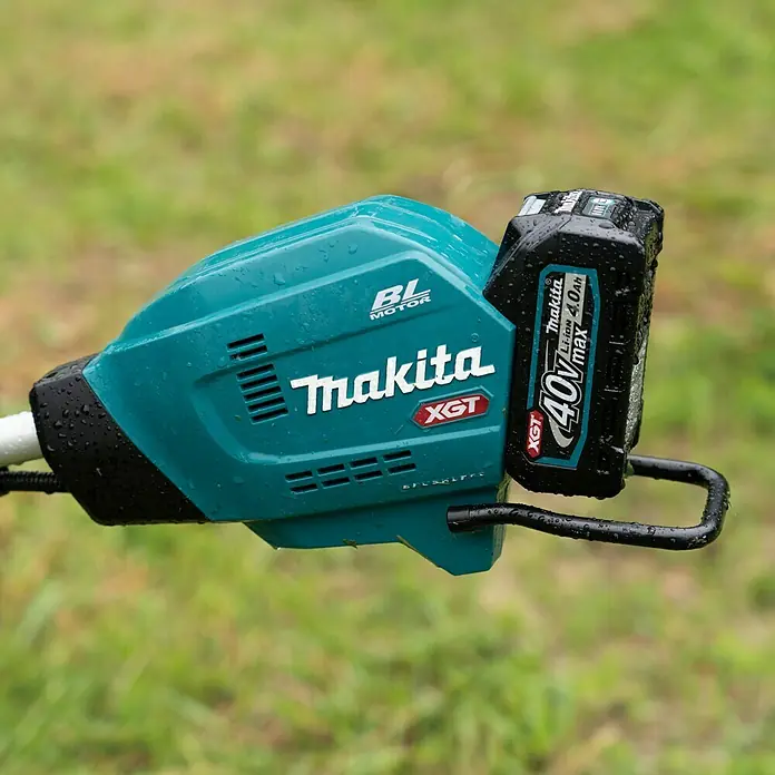 Makita XGT 40V max. Akku-Freischneider UR006GM102 - 40 V, 4 Ah, 1 Akku, Schnittbreite Faden: 43 cm, Schnittbreite Messer: 25,5 cm - Nahaufnahme eines Makita XGT Akku-Rasentrimmers mit einem 40V max Akku vor einem grünen Hintergrund.