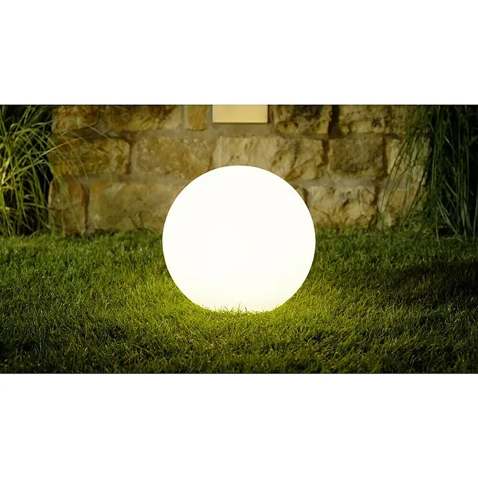 LED-Solar-DekoleuchteWeiß, 40 x 38 cm - Stimmungsvolle Gartenbeleuchtung: Eine leuchtende Kugel auf Rasen vor einer Steinmauer. Ideal für stimmungsvolle Abende im Freien.