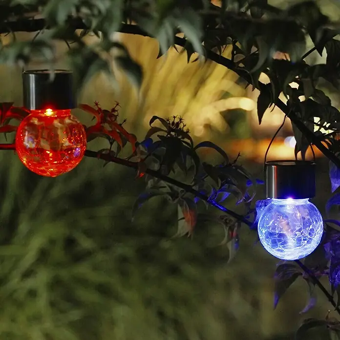 BAUHAUS Solar-Hängeleuchte - Nickel, Klar, IP44 - Zwei Solarleuchten mit Rissoptik hängen an einem Ast und beleuchten den Garten mit rotem und blauem Licht.