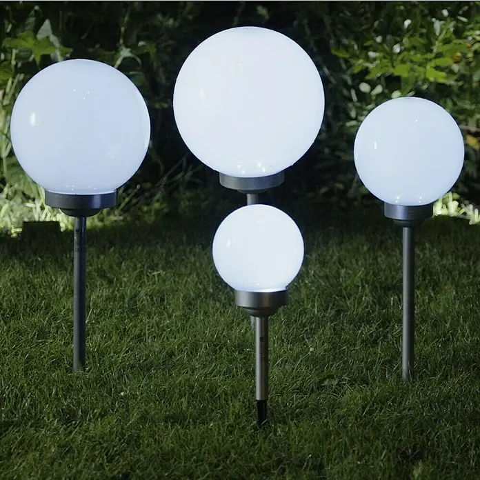 BAUHAUS Solar-Kugelleuchte Fara - Durchmesser: 30 cm, Höhe: 73 cm, LED - Eine Nahaufnahme von vier runden Gartenleuchten, die im Gras stehen und ein weiches, helles Licht ausstrahlen.