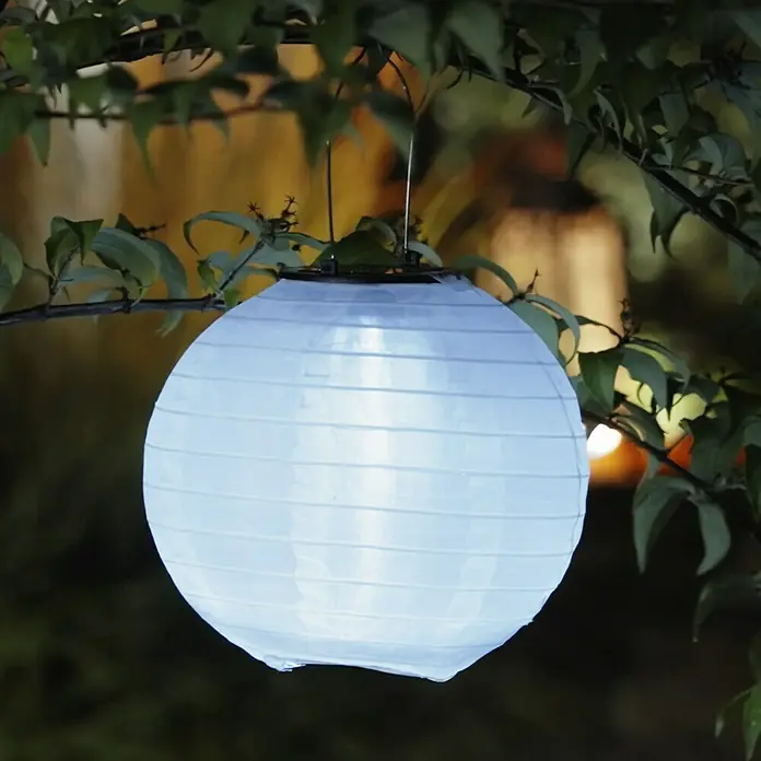 BAUHAUS Solarleuchte LampionWeiß, Leuchtdauer: 8 h - Diese Aufnahme zeigt eine strahlende, kugelförmige Papierlaterne, die an einem Baum hängt und mit ihrem sanften Licht eine warme Atmosphäre schafft.