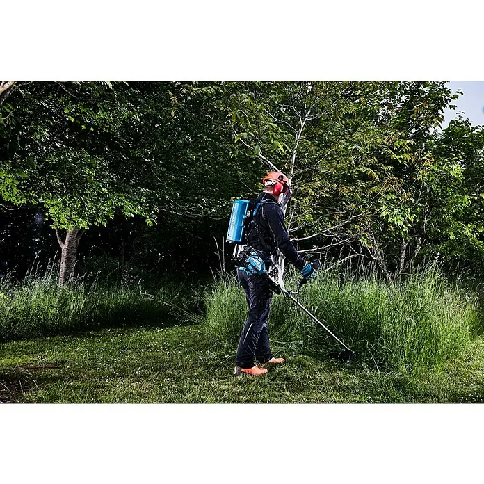 Makita LXT 18V Akku-Freischneider DUR369AZX6 - 18 V, Ohne Akku, Schnittbreite Faden: 43 cm, Schnittbreite Messer: 25,5 cm - Ein Gärtner mit einem Makita Akku-Rasentrimmer im Einsatz, der Unkraut in einem grünen Garten trimmt. Der Trimmer ist mit einem Akku-Rucksack verbunden.