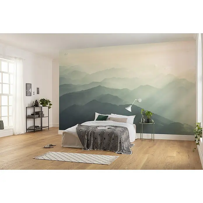 Komar Infinity 2 Fototapete Hazy HillsB x H: 400 x 250 cm, Vlies - Modernes Schlafzimmer mit einem Bett, einer gemusterten Tagesdecke und einer Wandtapete, die eine Berglandschaft zeigt.