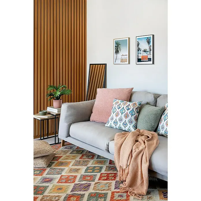 Alfombra de pelo corto Kilim Herat - Multicolor, 180 x 120 cm, 100% lana - Decoración de salón con un sofá gris, cojines, una manta y una alfombra colorida. Dos imágenes enmarcadas cuelgan de la pared sobre el sofá.