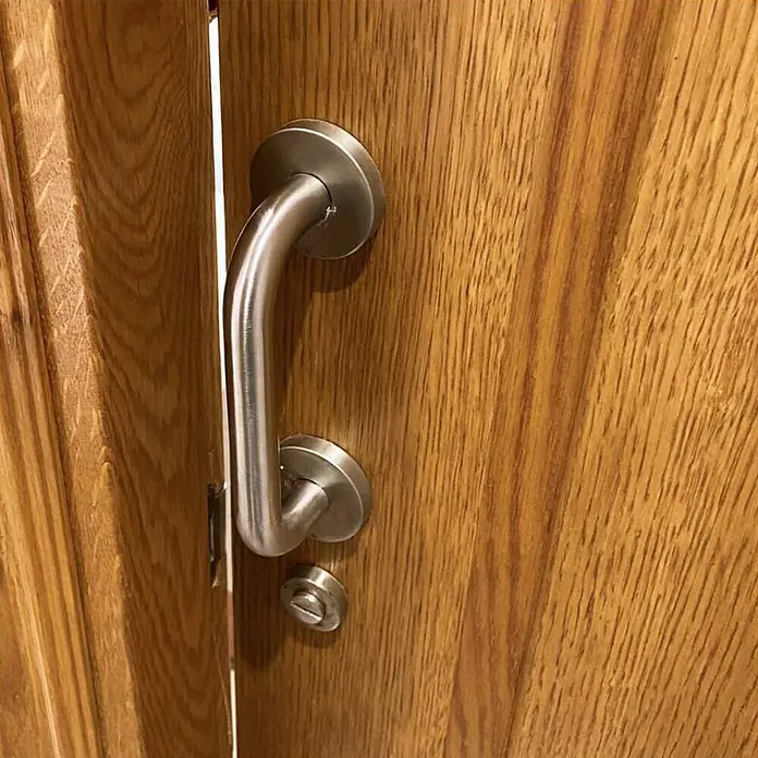 Micel Manillón 575 - Largo: 250 mm, Plateado, Curvado - Primer plano de una puerta de madera con un moderno tirador curvo y un pequeño pomo giratorio debajo.