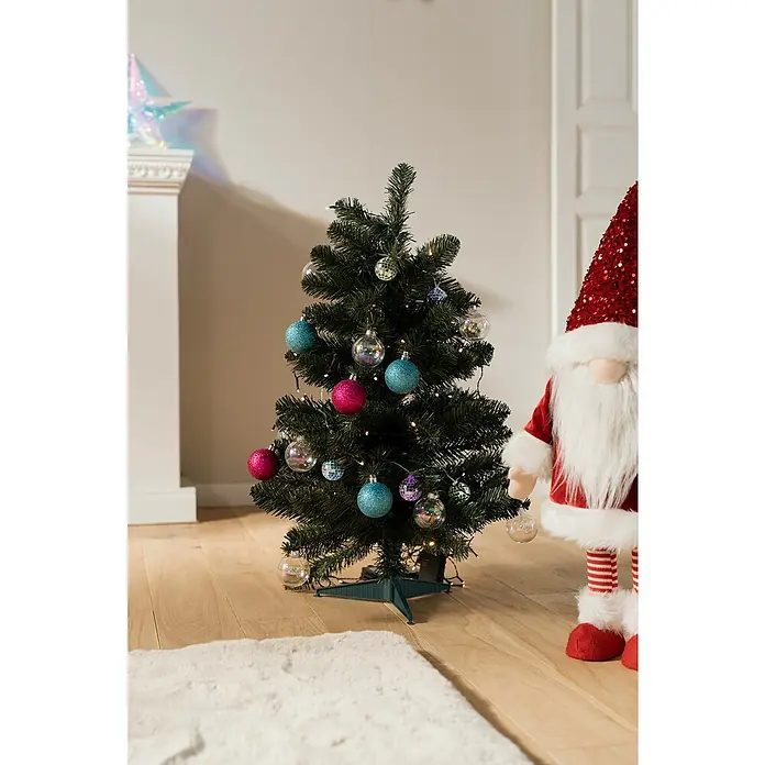 Künstlicher Weihnachtsbaum Allison - Höhe: 60 cm, Grün, LED-Beleuchtung - Geschmückter Weihnachtsbaum mit bunten Kugeln und Lichtern, neben einem Weihnachtsmann auf einem Holzboden.