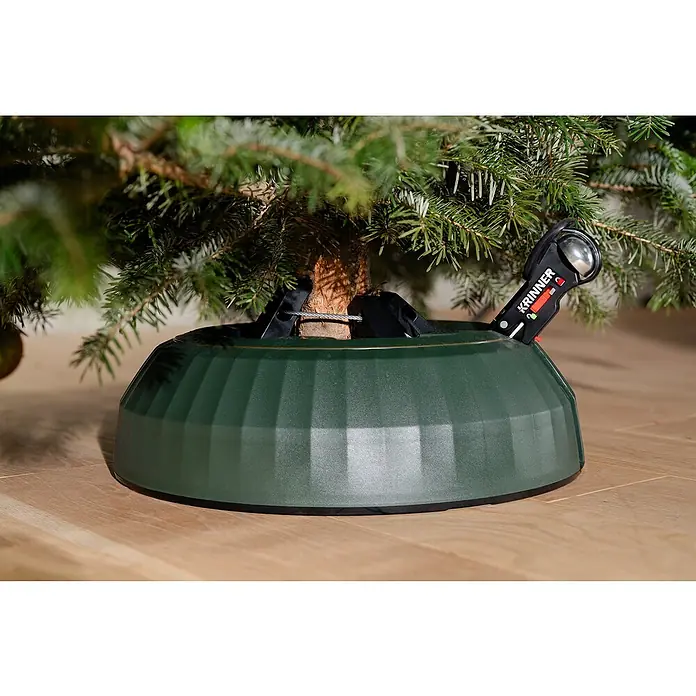 Krinner Christbaumständer X-320 Deluxe - Rund, Max_Baumlaenge: 3,2 Meter (m) - Nahaufnahme eines grünen Christbaumständers mit dem Schriftzug "KRINNER" unter einem Weihnachtsbaum.