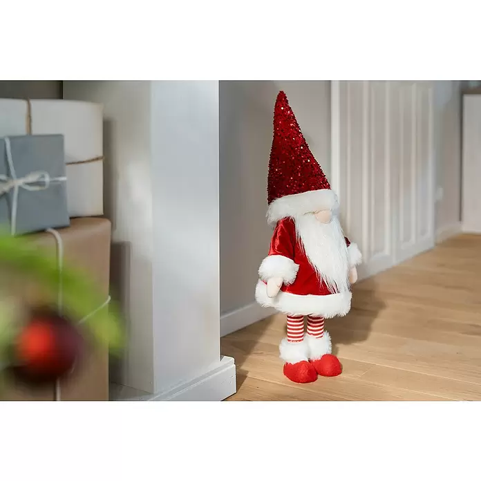 Dekofigur Weihnachtswichtel schaukelnd - L x B x H: 33 x 33 x 83 cm, Polyester - Ein stehender Weihnachtswichtel mit rotem Paillettenhut, rotem Samtmantel, weißem Bart, gestreiften Socken und roten Schuhen in festlicher Innenumgebung.