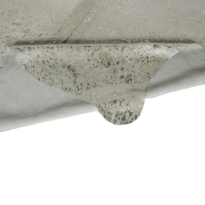 Esbeco Kuhfell Gefleckt - Silber, 100 % Echtfell - Nahaufnahme eines strukturierten, grauen Tierfells. Die Oberfläche weist ein einzigartiges Punktmuster und eine zurückgebogene Kante auf.