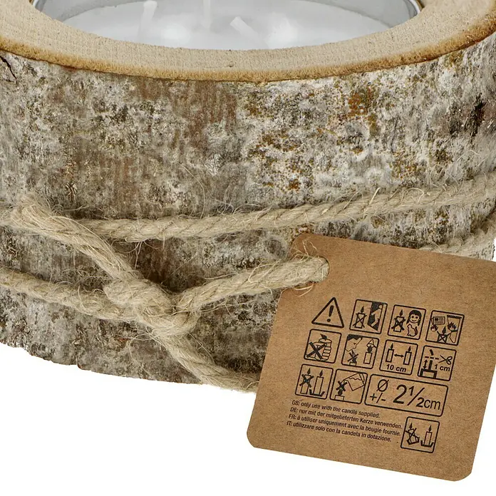 Windlicht mit Kerze - Weiß/Natur, Ø x H: 16 x 8 cm - Detailansicht eines rustikalen Kerzenhalters aus Holz mit einer Banderole und einem Anhänger mit Sicherheitshinweisen.
