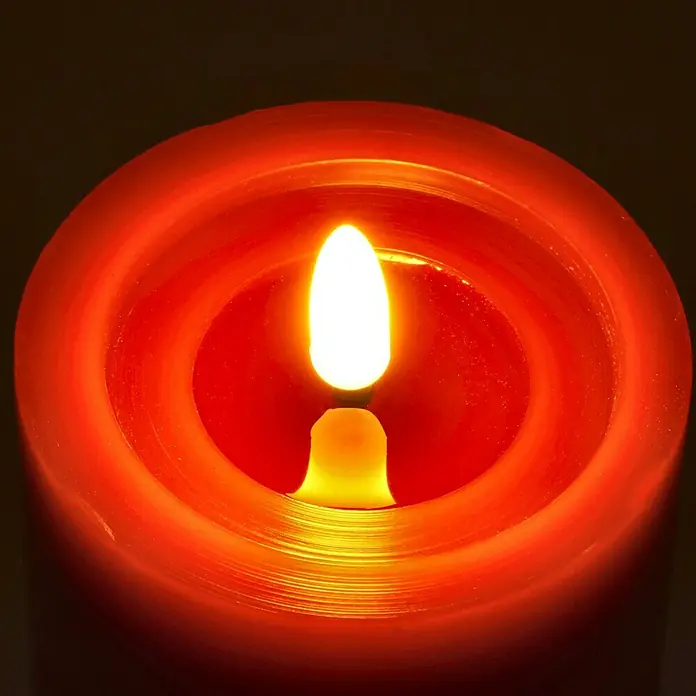 LED-Kerze Shine - Rot, Ø x H: 7,5 x 10 cm, Echtwachs - Nahaufnahme einer brennenden roten Stumpenkerze. Das warme Licht der Flamme erzeugt eine gemütliche Atmosphäre.