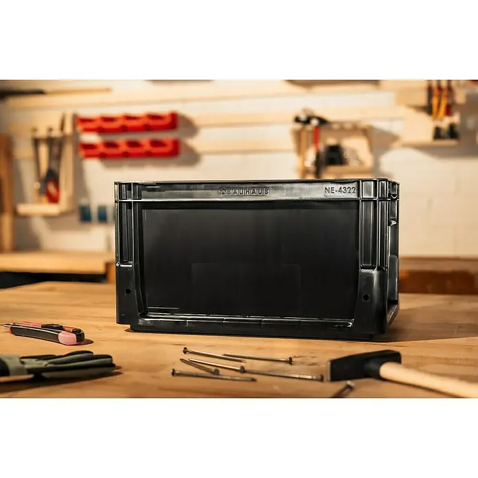 BAUHAUS Eurobox - L x B x H: 40 x 30 x 22 cm, 21 l, Schwarz - Werkstatt-Szene mit einer schwarzen Bauhaus-Box im Fokus, umgeben von Werkzeugen wie Hammer, Nägeln und einem Cutter.