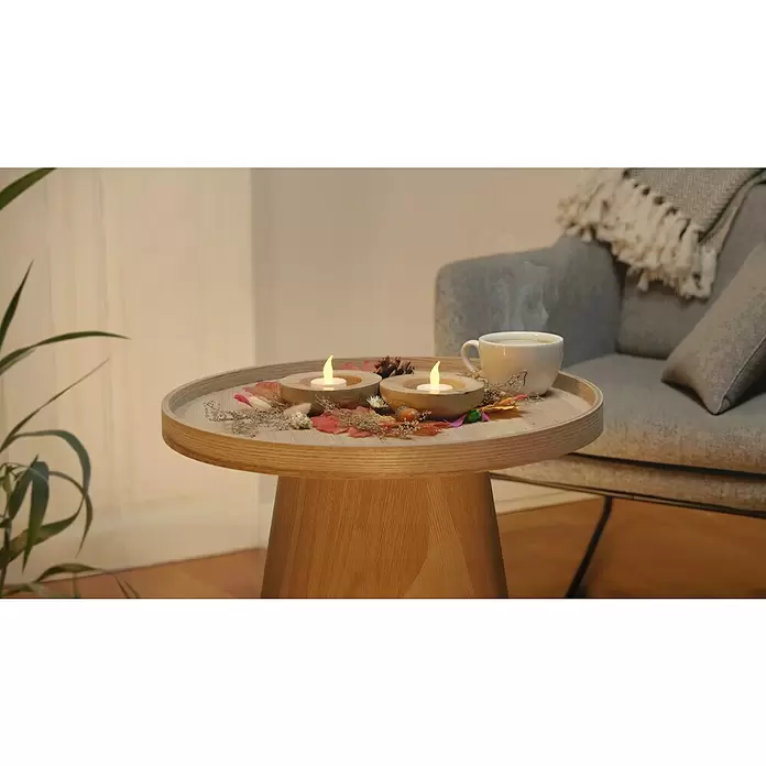 LED-Teelicht - 2 Stk., Durchmesser: 4 cm - Heller Holztisch mit Tablettplatte, dekoriert mit Kerzen und Blättern, neben einem Sessel.
