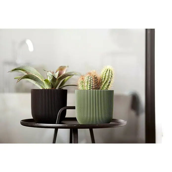 Capi Europe Übertopf rund Nature GrooveAußenmaß (Ø x H): 14 x 13 cm, Grün, Polyester - Zwei Pflanzen, eine Sukkulente und ein Kaktus, in gerippten Töpfen auf einem schwarzen Beistelltisch, der eine moderne und stilvolle Dekoration bietet.