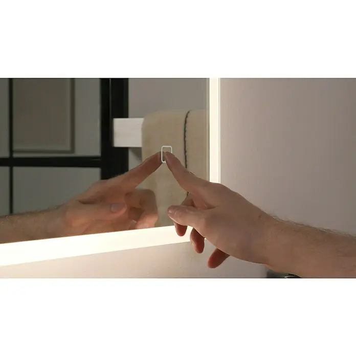 Riva LED-Lichtspiegel Draw Tape - 100 x 75 cm - Eine Hand berührt den Touchscreen eines beleuchteten Spiegels im Badezimmer, um die Lichtfunktionen zu steuern.